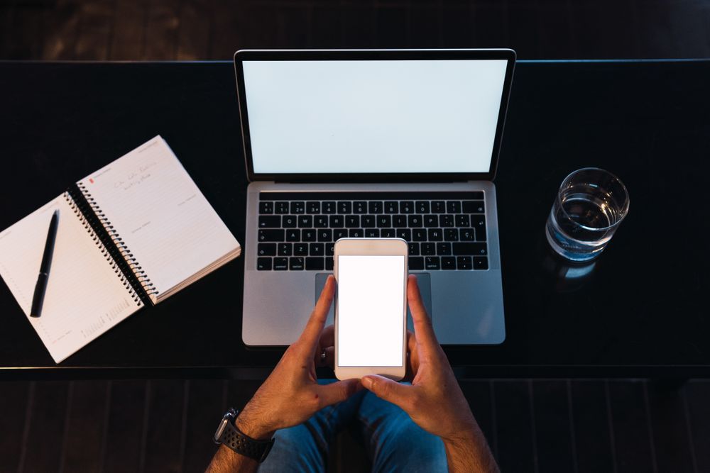 Anonymous man browsing smartphone near laptop