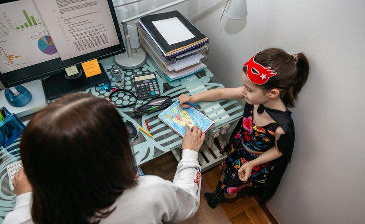 Woman teleworking with daughter showing her a drawing