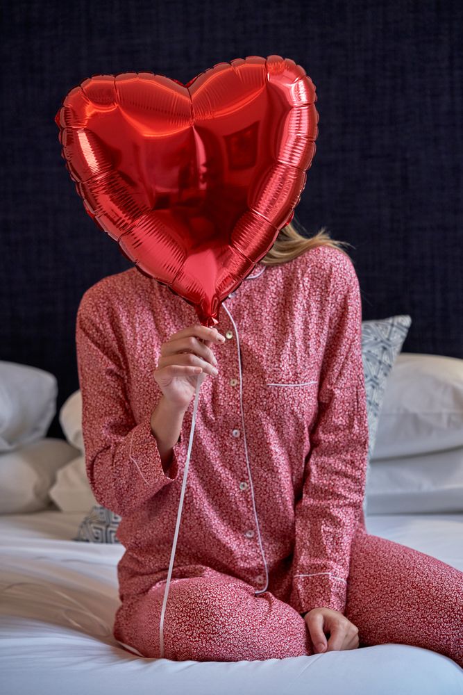 Young woman hiding face behind red heart balloon