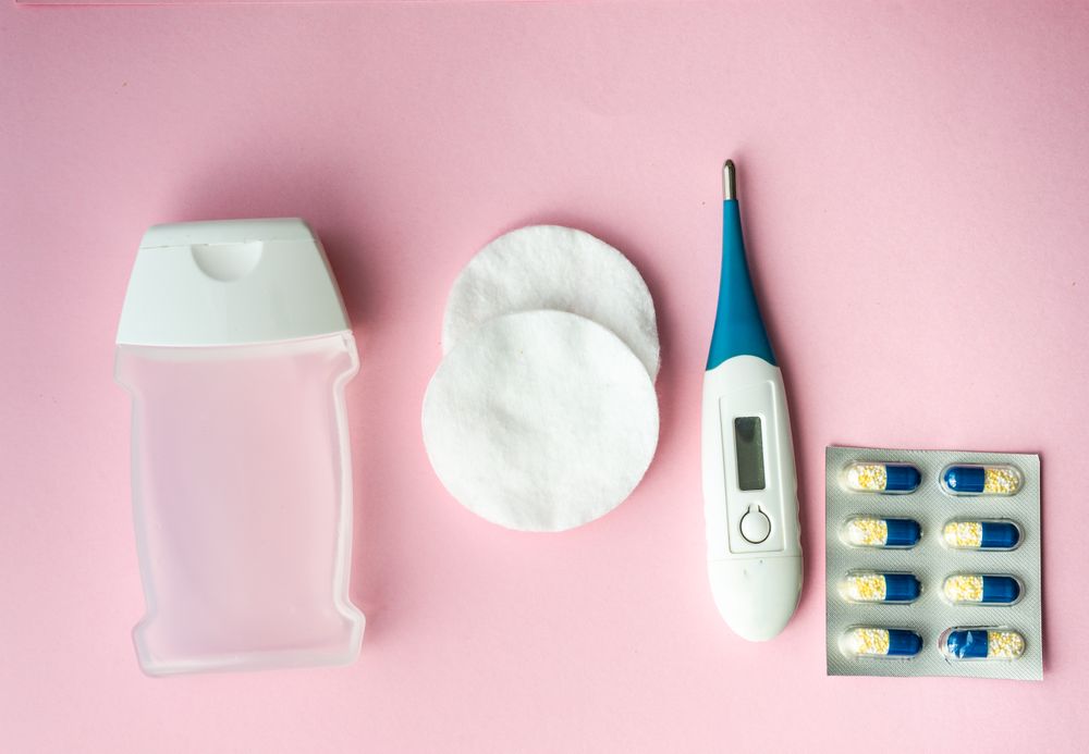 Looking down at pink table with pills, cotton, digital thermometer and hand soap
