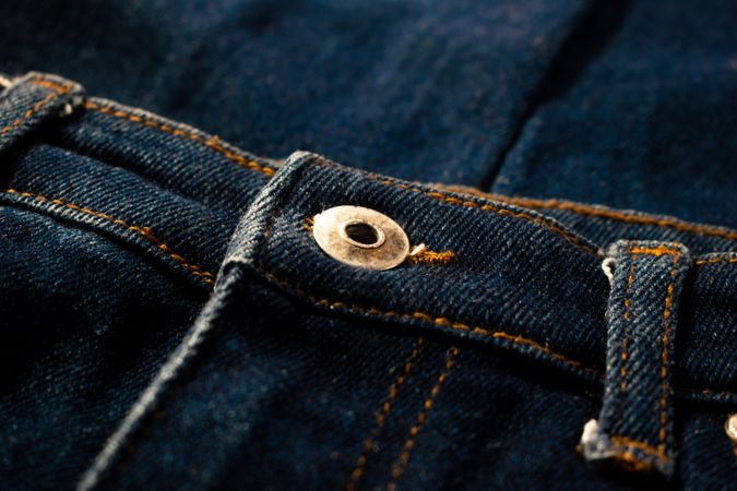 Close up gold and shiny button navy blue jeans fabric background texture.