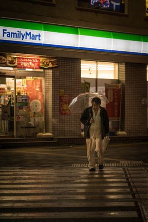 Man in dark jacket holding umbrella walking on sidewalk at night
