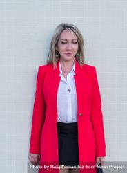 Portrait of a blonde woman wearing red jacket and skirt against a tiled wall 0LdE6r