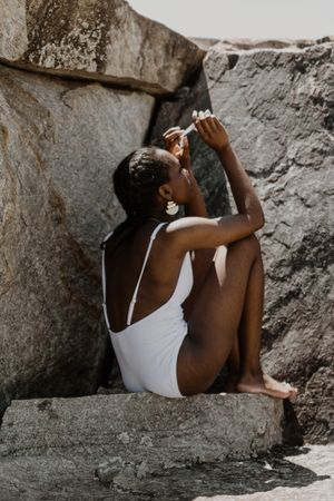 Back view of woman swimsuit sitting on a rock