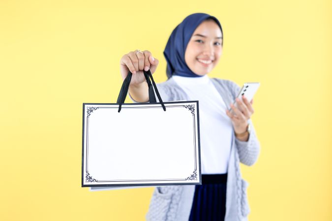 Asian Muslim Woman in Grey Sweater and Hijab Holding Blank Shopping Bag