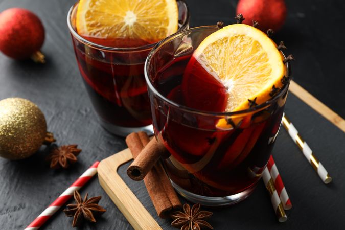 Glasses of tasty mulled wine and christmas baubles on dark background, close up