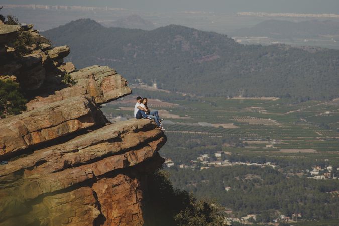 Distant loving couple embracing while sitting on high cliff