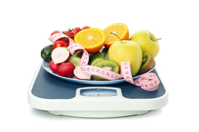 Scales, measuring tape and vegetarian food isolated on blank background