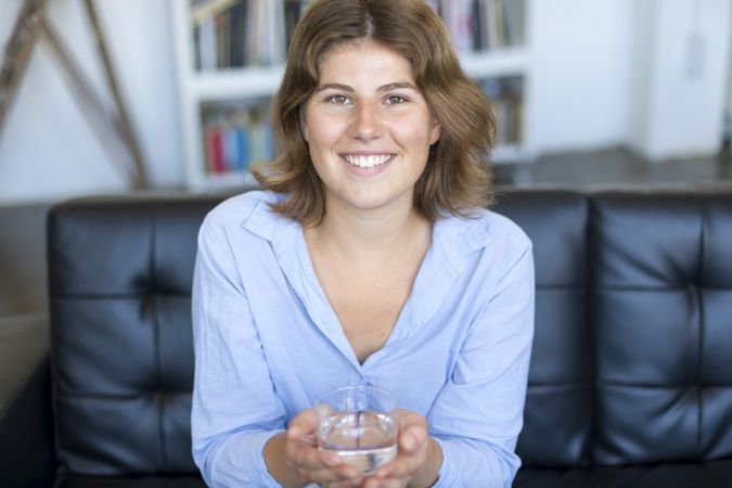 Female drinking water sitting on a couch at home and looking at camera