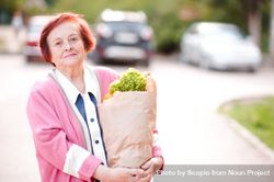 Older woman holding grocery bag standing on street 5rKrM4