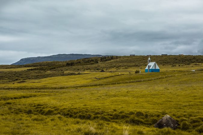 Small house in green filed under cloudy sky