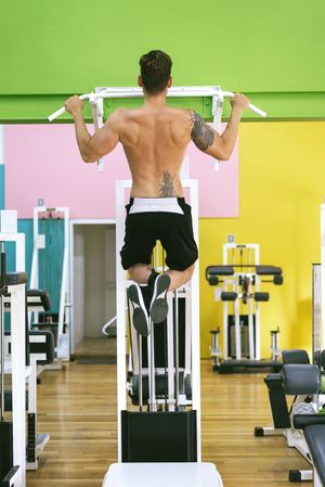 Back of man working out upper body in a fitness club on pull up bar