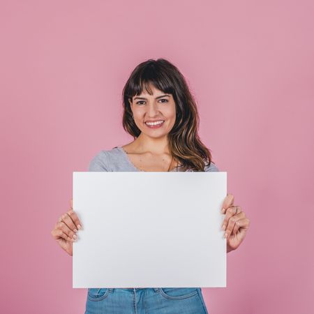 Smiling woman holding a blank sign against a pink background