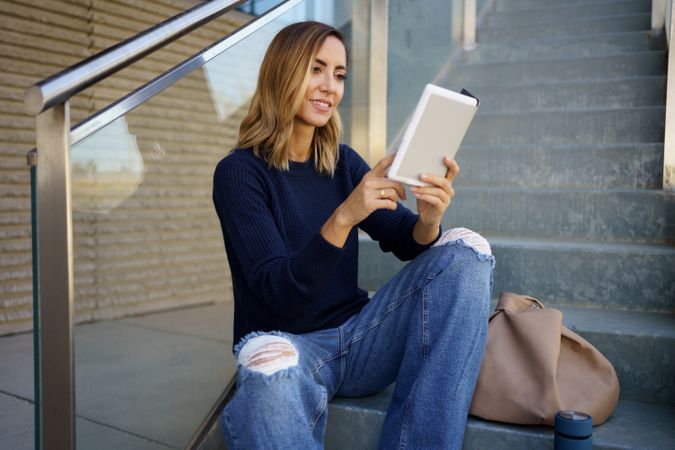 Happy woman reading e book on steps