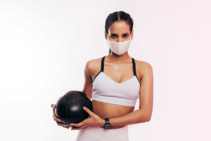 Woman holding medicine ball and wearing a face mask