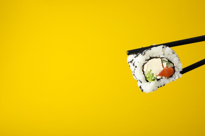 Chopsticks with sushi roll on yellow background, space for text. Japanese food