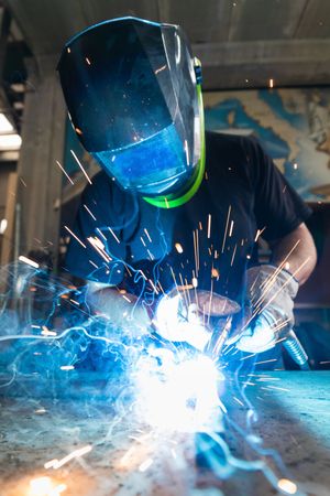 Welder in protective helmet welding metal detail in workshop
