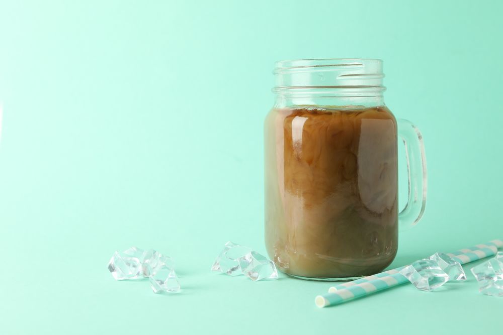 Jar of ice coffee, ice cubes and straws on mint background