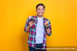 Thrilled Asian man smiling while holding wallet and making fist 47d9rb