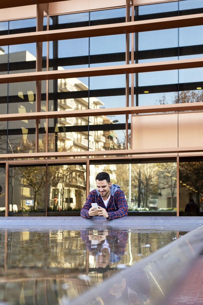 Man with smartphone by reflective city fountain