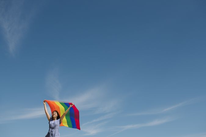 Young woman with rainbow banner against sky