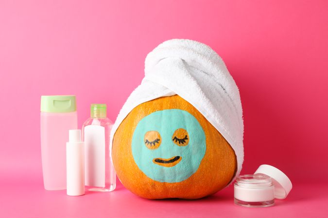 Funny pumpkin and skin care accessories on pink background, space for text
