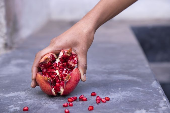Hand holding pomegranate fruit in hand on stone background, close up