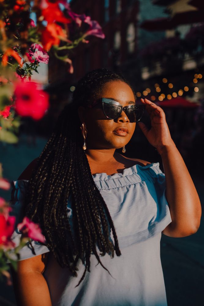 Joyful trendy Black woman in sunglasses standing beside blossomed tree