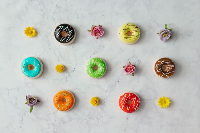 Rows of colorful donuts and flowers on marble background