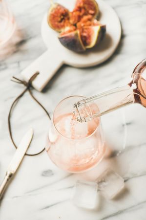 Rose wine being poured in glass of wine on marble table with quartered fig