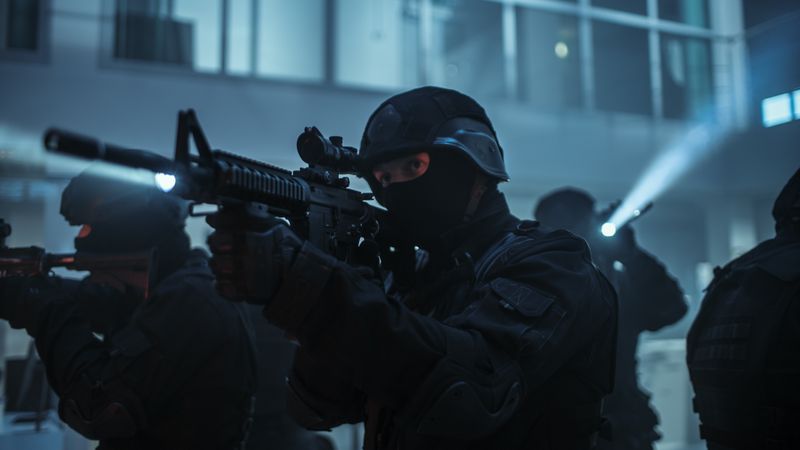 Masked Squad of Armed SWAT Police Officers Stand in Dark Seized Office Building with Desks and Computers.