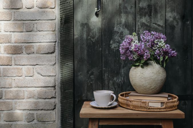 Lilacs, wicker tray, books against brick wall in sunlight