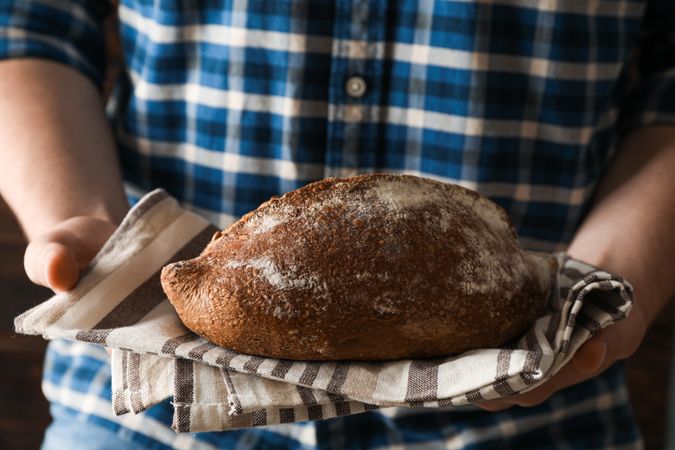Male hands hold wheat bread against wooden background, space for text