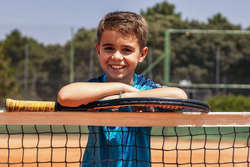 Little boy playing tennis on a dirt court