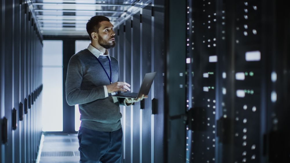 IT Technician Works on Laptop next to a Server Cabinet in Big Data Center.