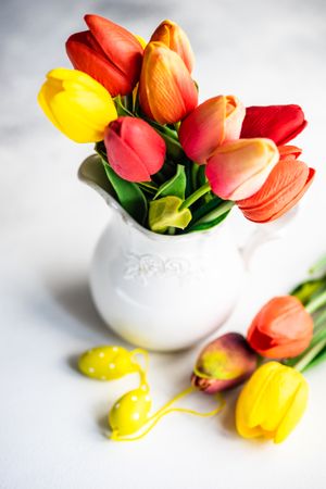 Easter concept of tulips in vase with yellow egg ornaments