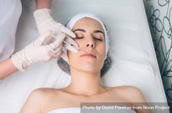 Aesthetician's hand's in latex gloves injecting filler into female's lips in a beauty salon bGRvoY