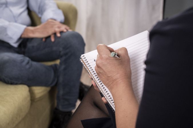 Therapist taking notes while listening to a patient during a session.