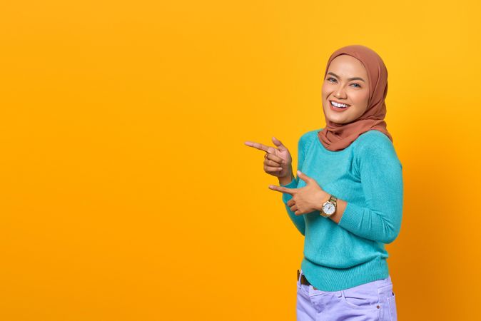 Happy Muslim woman pointing to her side in studio