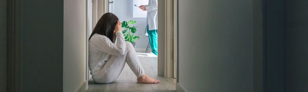 Patient sitting on the floor in the corridor of a mental health center with a doctor in the background