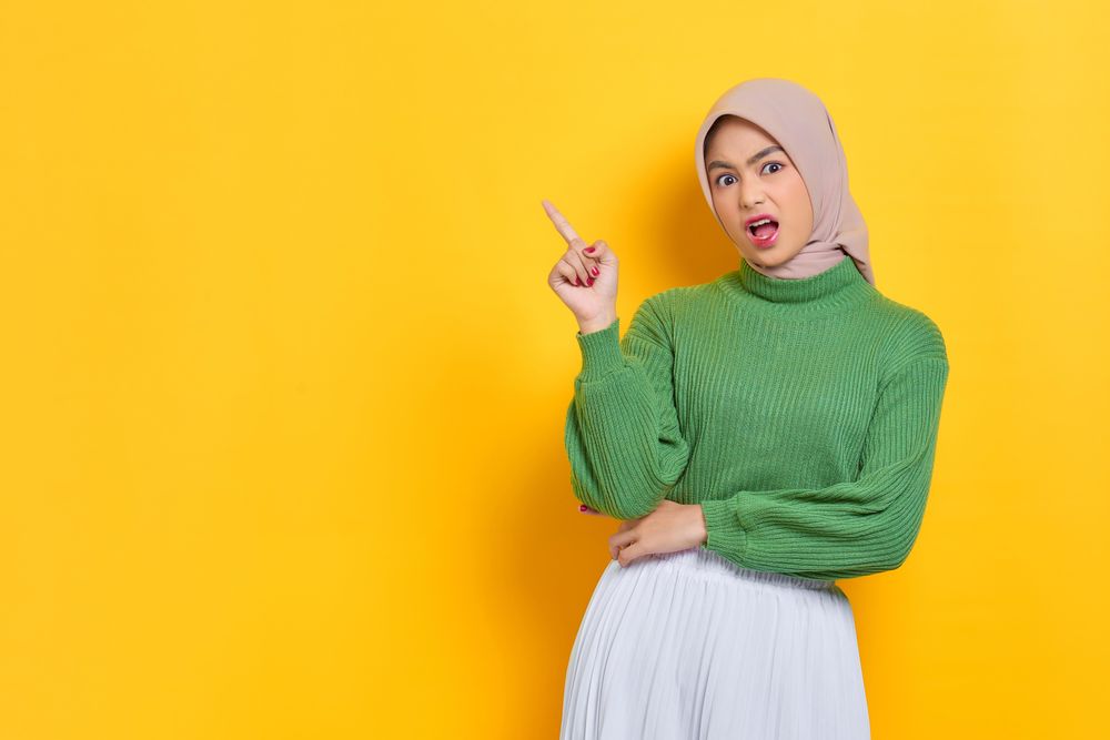 Amazed woman in headscarf pointing up to the side