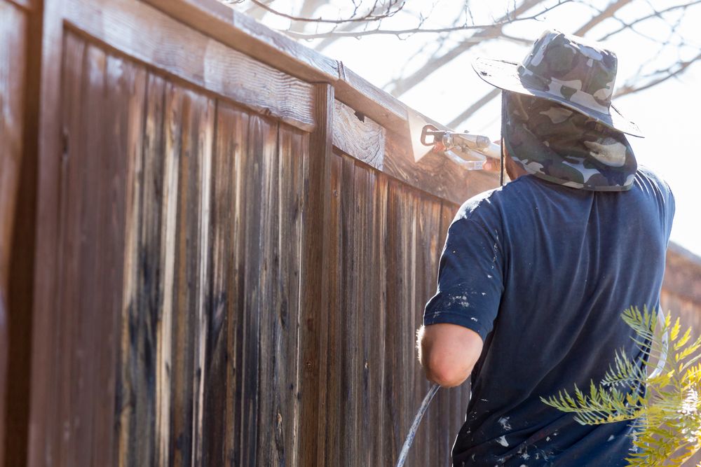 Professional Painter Spraying Yard Fence with Stain