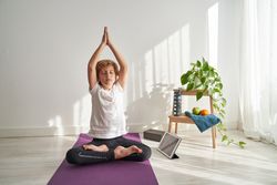 Boy meditating with raised arms in Padmasana at home