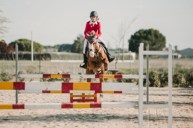 Teen girl riding horse and jumping over bars