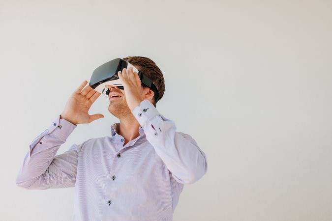 Happy young man using the virtual reality headset against grey background with copy space