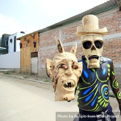 Man with skull face mask holding a mask standing outdoor in a village in Oaxaca, Mexico 0gqnM4