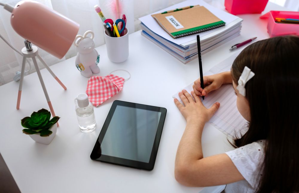 Girl studying at home with tablet and mask on table