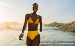 Attractive woman in yellow bikini walking along the beach 4MKAr0