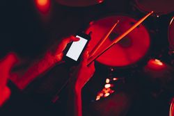 Man with drumsticks using smartphone near drums in redness