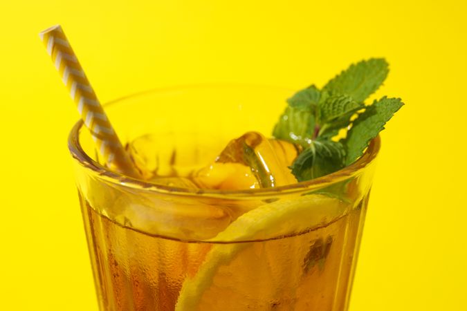 Cold tea with orange slices and mint leaves on a yellow background